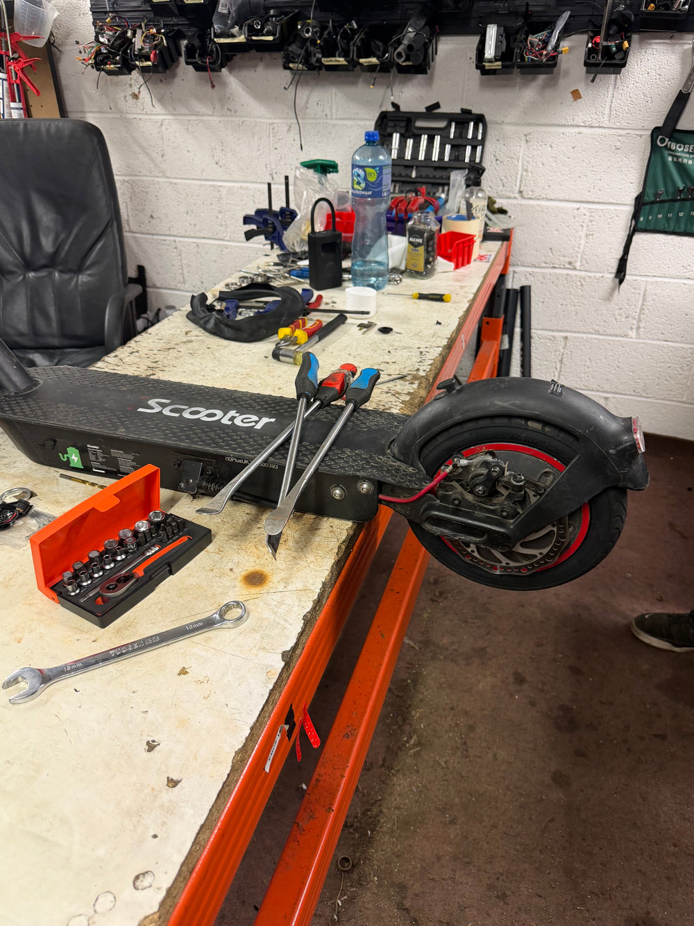 Electric scooter rear wheel and deck on the Yocks repair bench with tyre levers, sockets and spanners